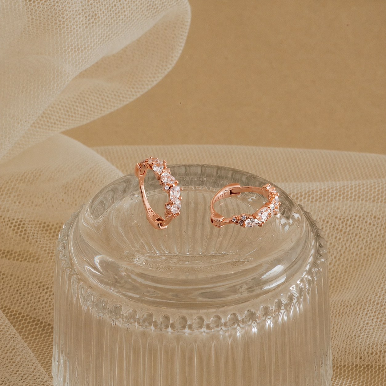 Rose gold rings with gemstones on a clear glass stand against a beige fabric background